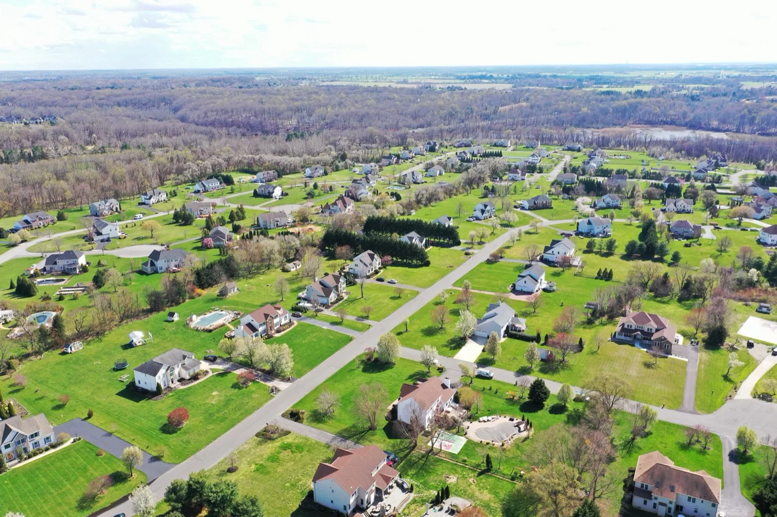 An aerial of single family homes on large lots, with fields and woods beyond